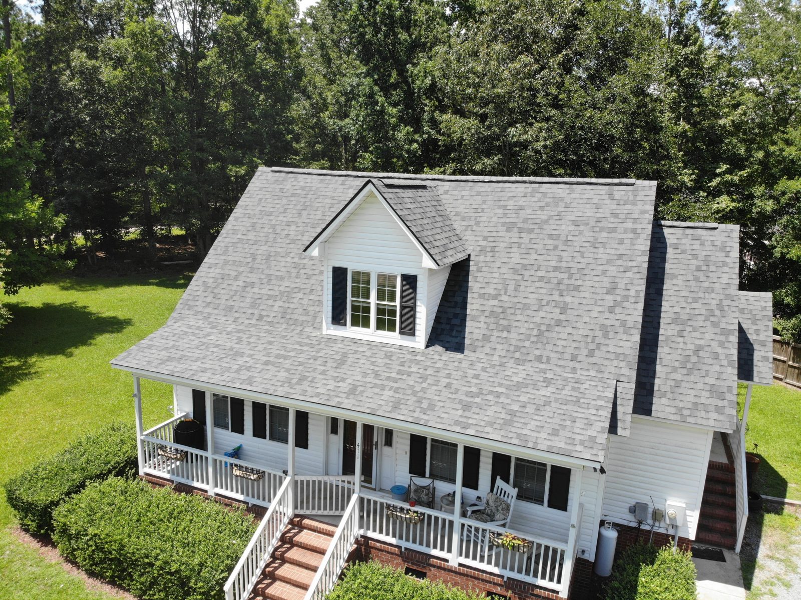 Completed white farmhouse with a new gray architectural shingle roof and covered front porch in Lexington, South Carolina
